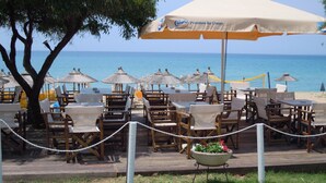 Un restaurante frente a la playa con terraza, sombrillas y vistas al mar.