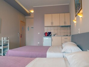 A hotel room with two beds, a kitchenette, a small desk, and a chair.