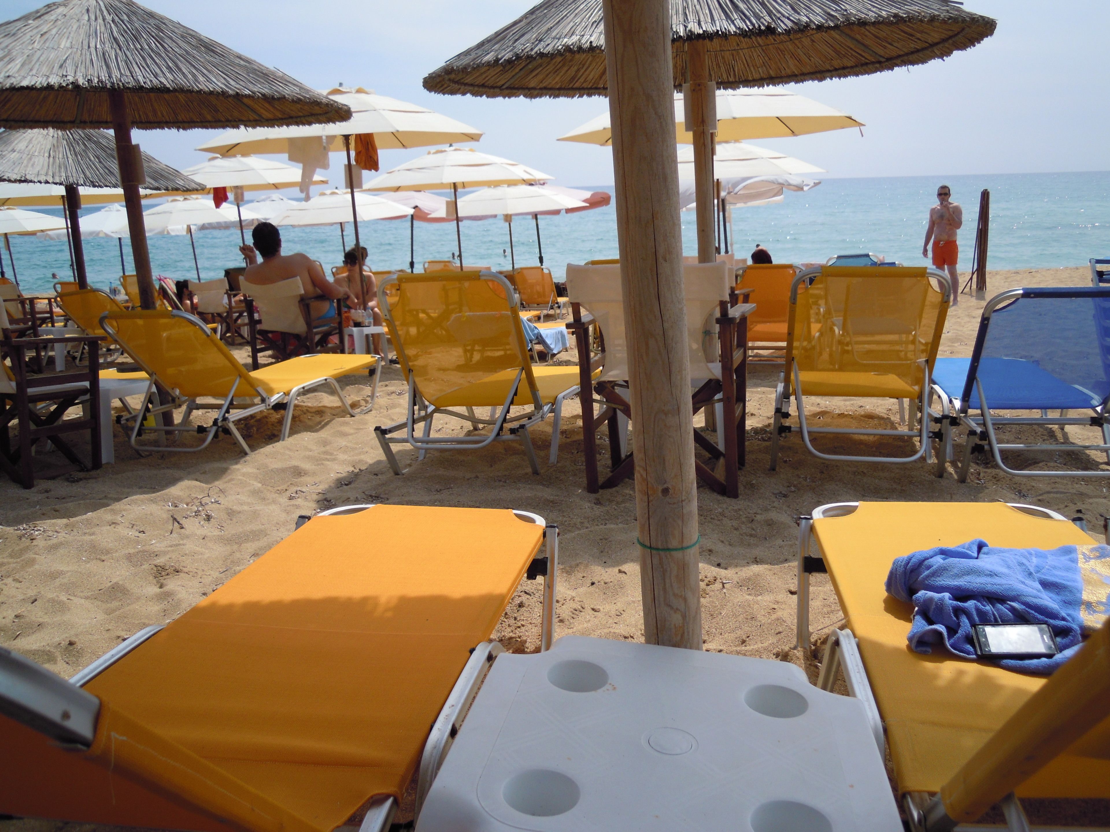 Une plage avec des transats jaunes et blancs, des parasols et un poteau en bois au premier plan.