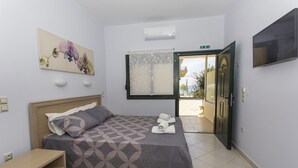 Una habitación de hotel con una cama, un escritorio pequeño, un cuadro, un equipo de aire acondicionado y una puerta que da a un balcón.