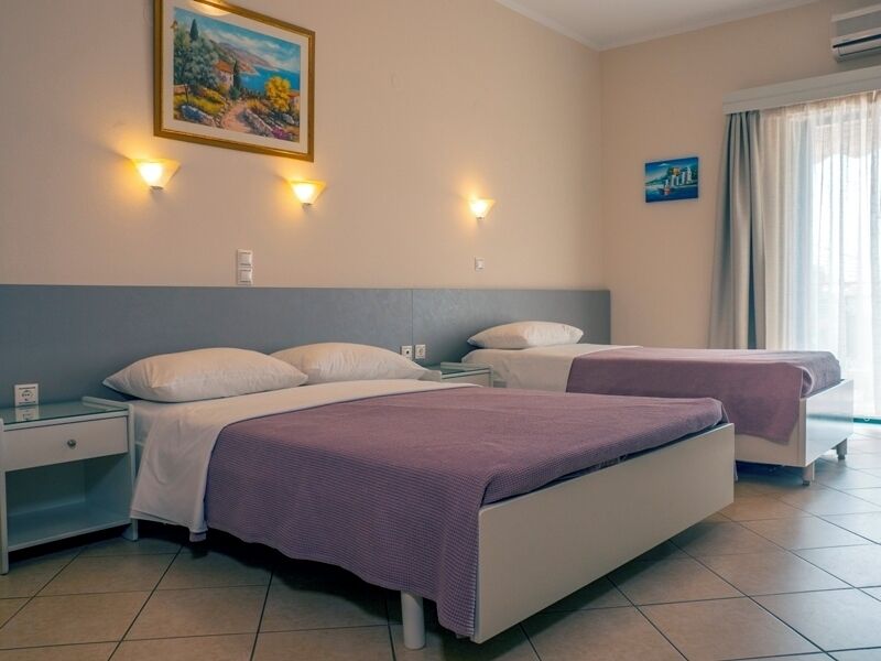 Habitación de hotel con dos camas, una mesita de noche, un cuadro colgado en la pared y una ventana con cortinas.