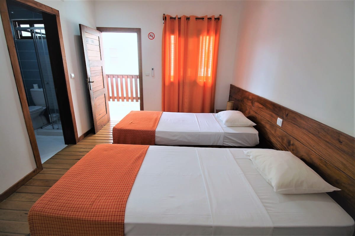 A room with two beds, a wooden headboard, a balcony door, and a view of the outside.