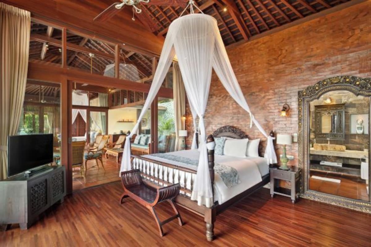 A spacious bedroom with a four-poster bed, wooden flooring, and a large mirror.