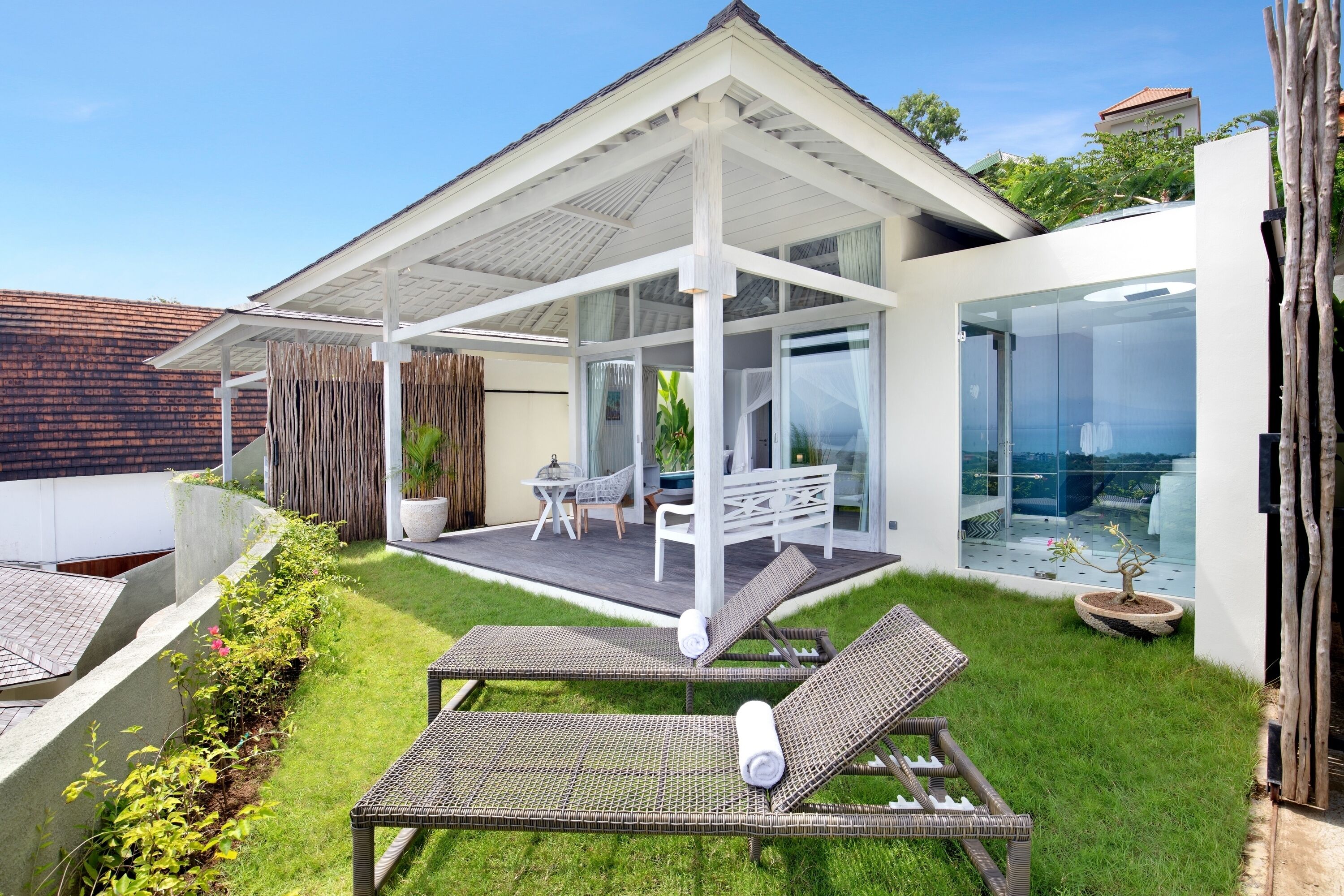 A modern house with a covered patio, two lounge chairs, a dining table, and a potted plant.