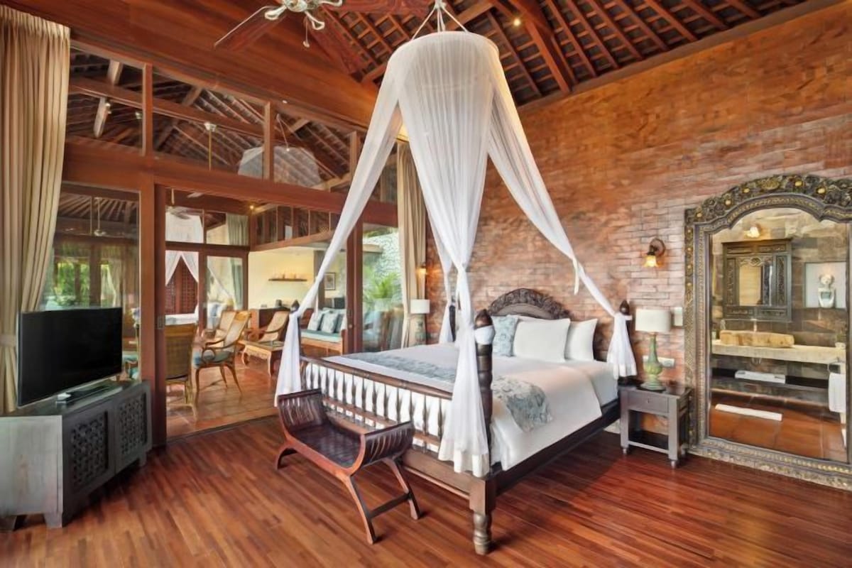 A spacious bedroom with a four-poster bed, wooden flooring, and a large mirror.