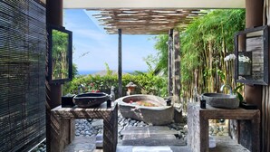 A serene outdoor spa area with a stone hot tub, wooden benches, and a view of the ocean. - Hidden Hills Villas - Small Luxury Hotels of The World (Pecatu)
