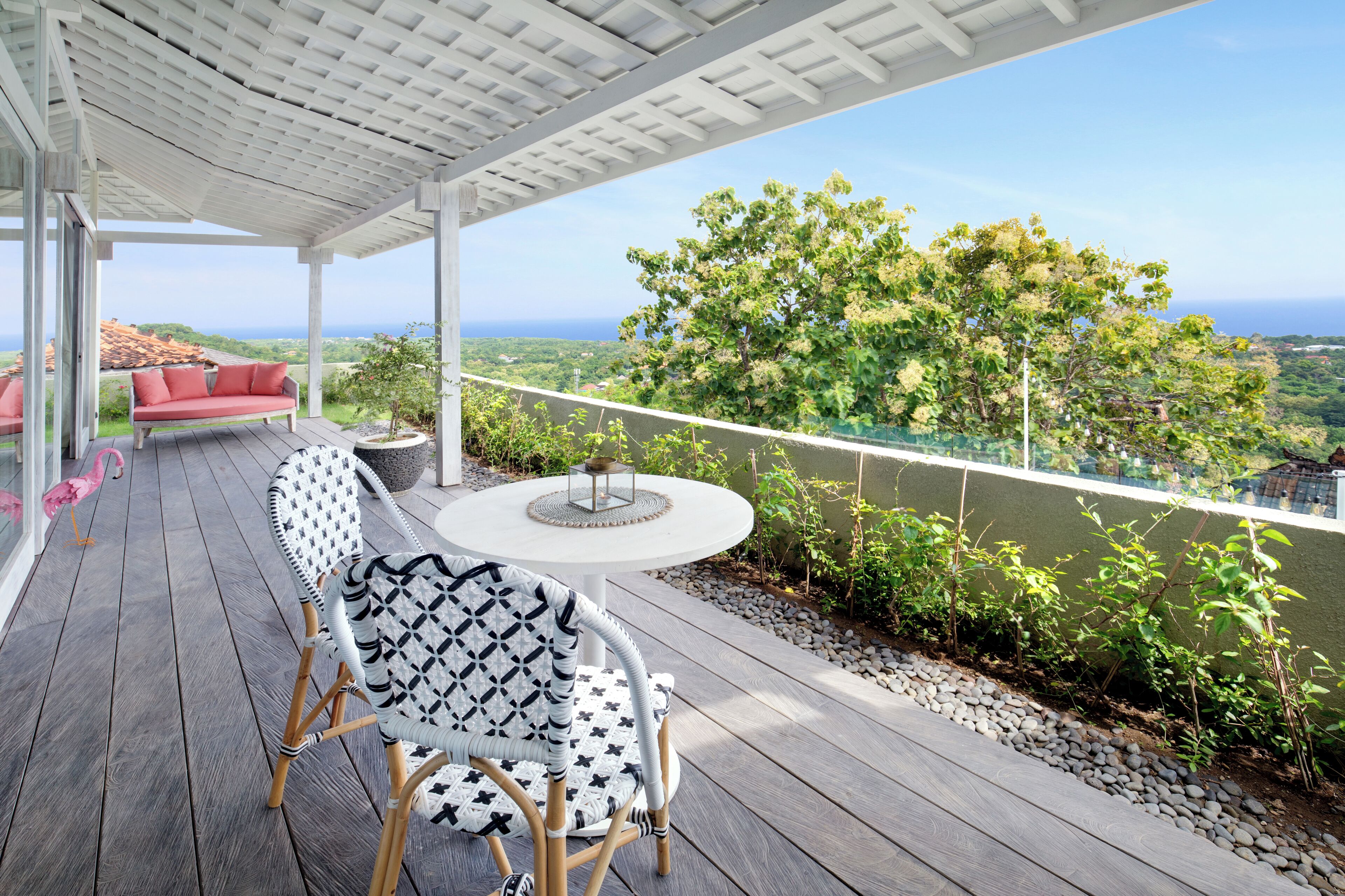 Un espacio al aire libre cubierto con una mesa y sillas blancas, un sofá rojo y vistas al océano y la vegetación.