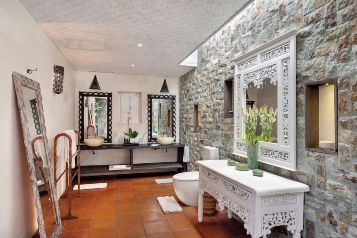 A bathroom with a stone wall, a white vanity, and two large mirrors.