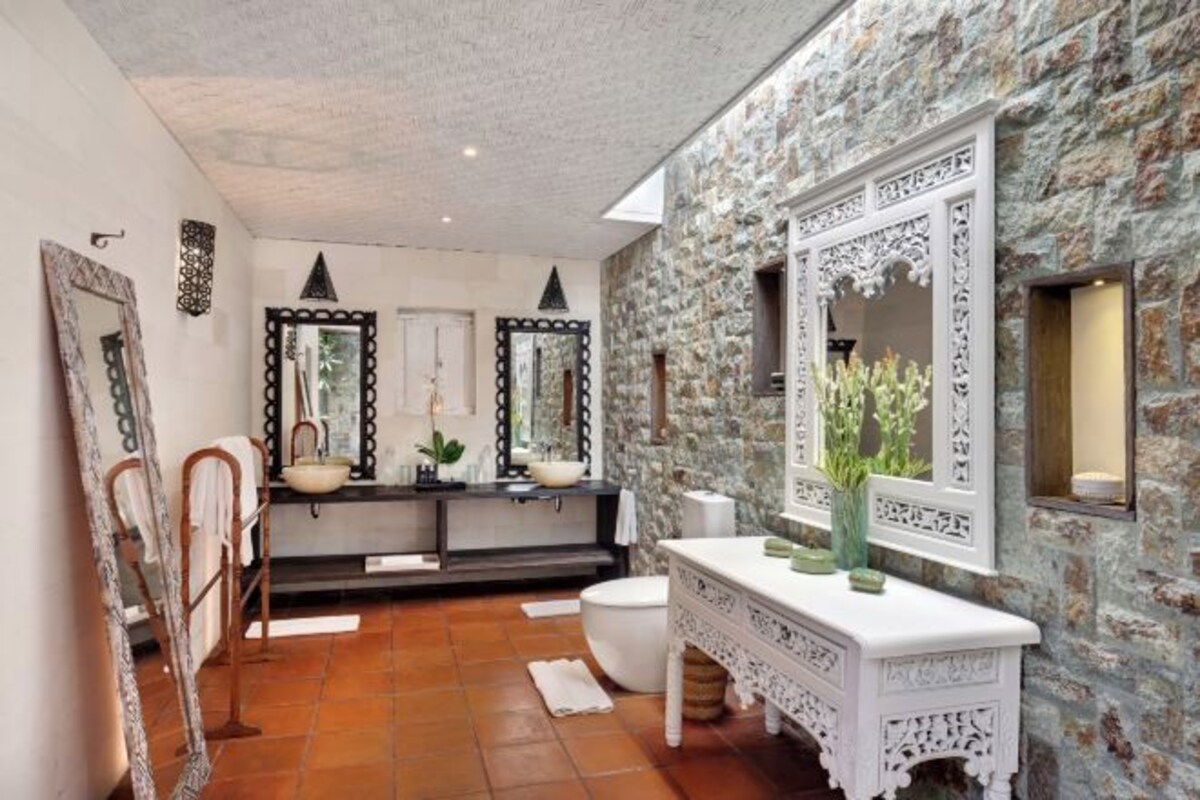 A bathroom with a stone wall, a white vanity, and two large mirrors.