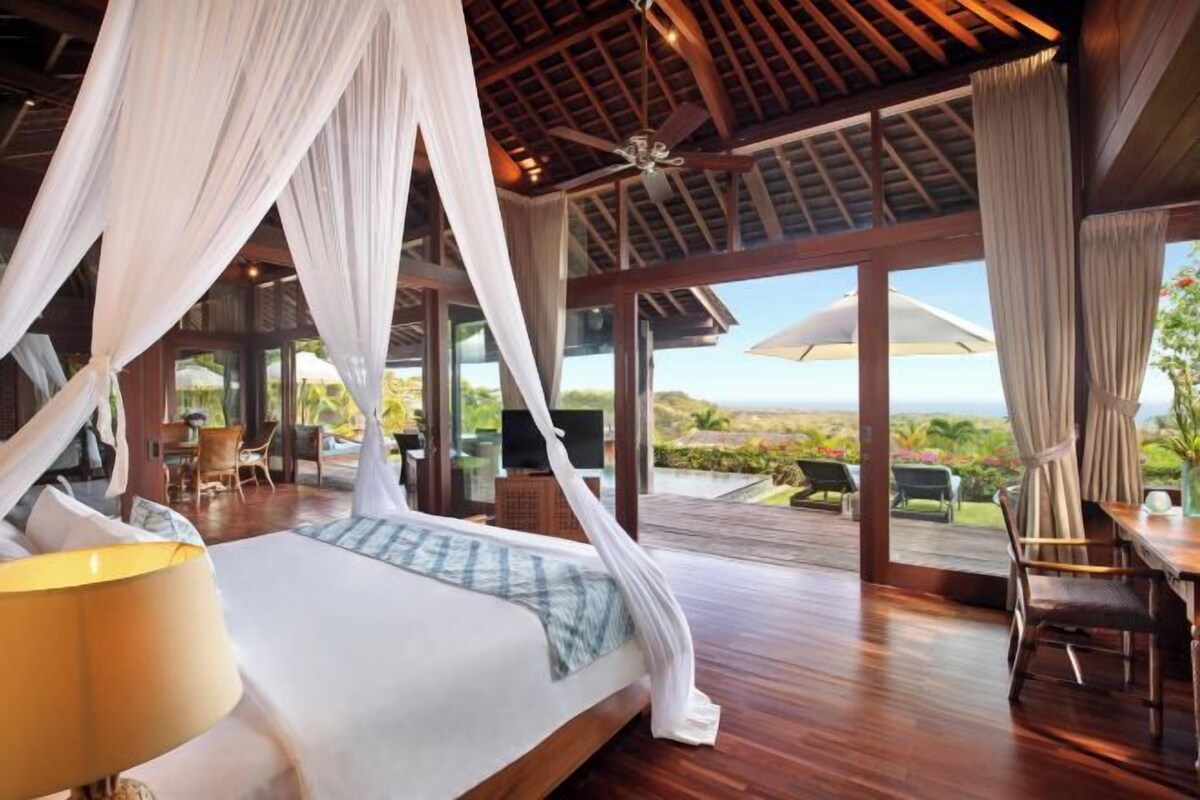 A spacious bedroom with a large bed, a ceiling fan, and a view of the landscape.