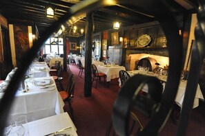 An indoor dining area with tables set for service, wooden beams on the ceiling, and framed artwork on the walls.