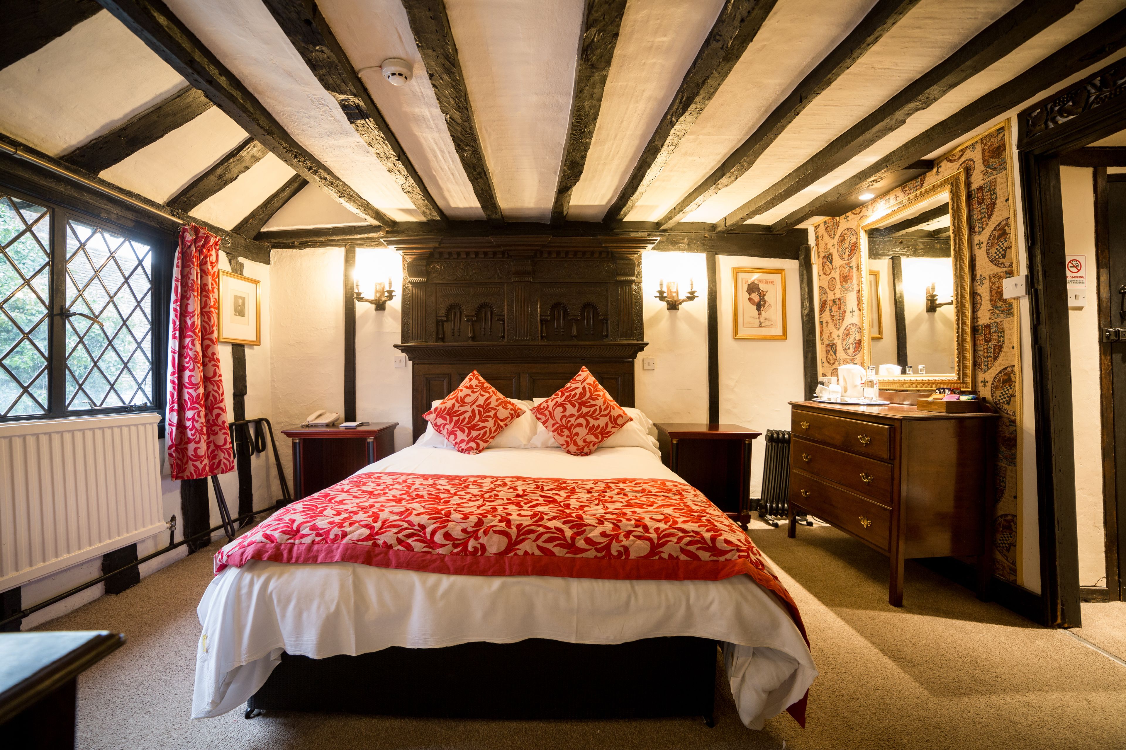 A traditional room with a large bed, wooden beams on the ceiling, a dresser, and a mirror.