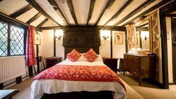 Quarto tradicional com uma cama grande, vigas de madeira no teto, uma cômoda e um espelho.