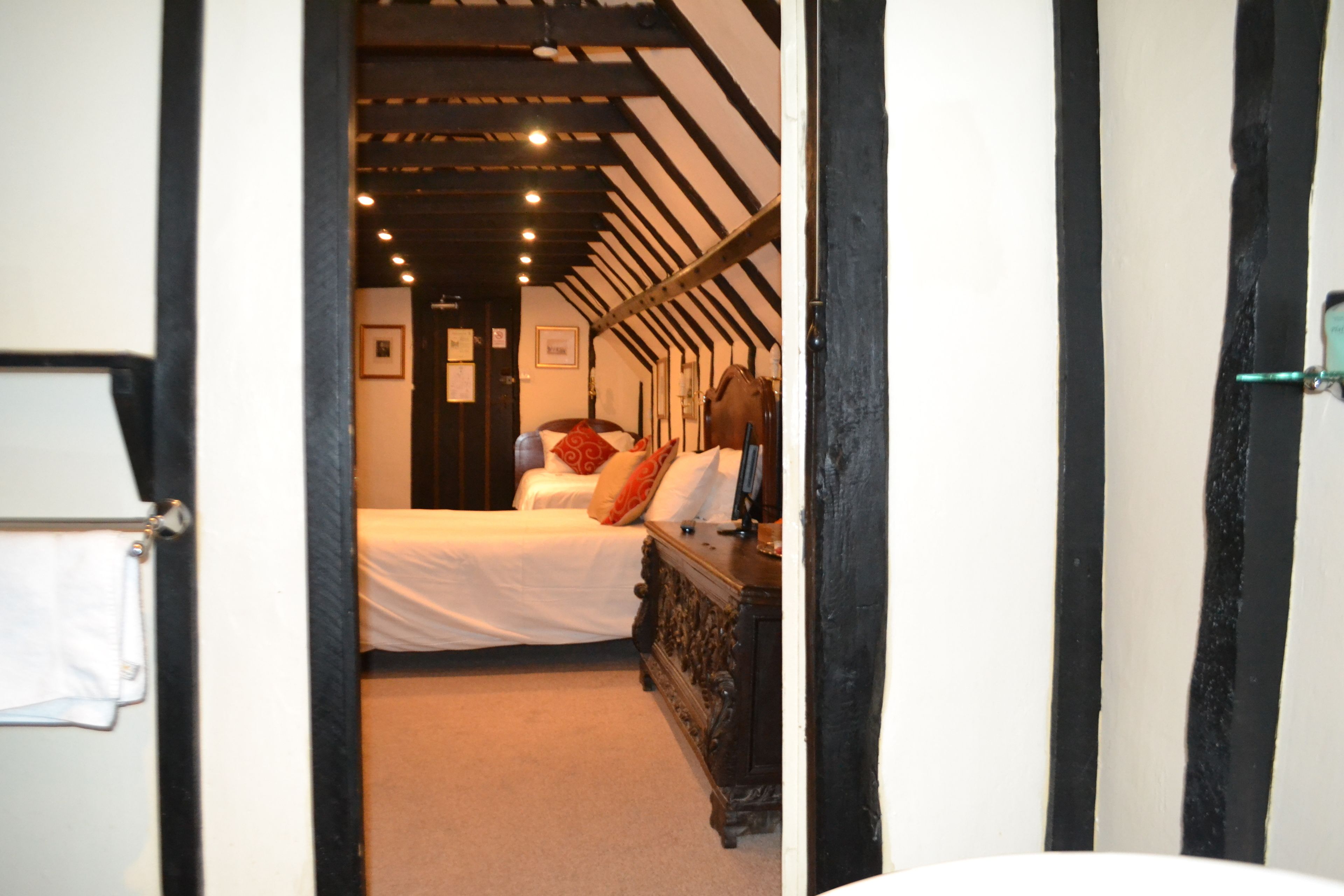 A narrow hallway leading to a bedroom with a bed, a dresser, and a door with a towel hanging on it.