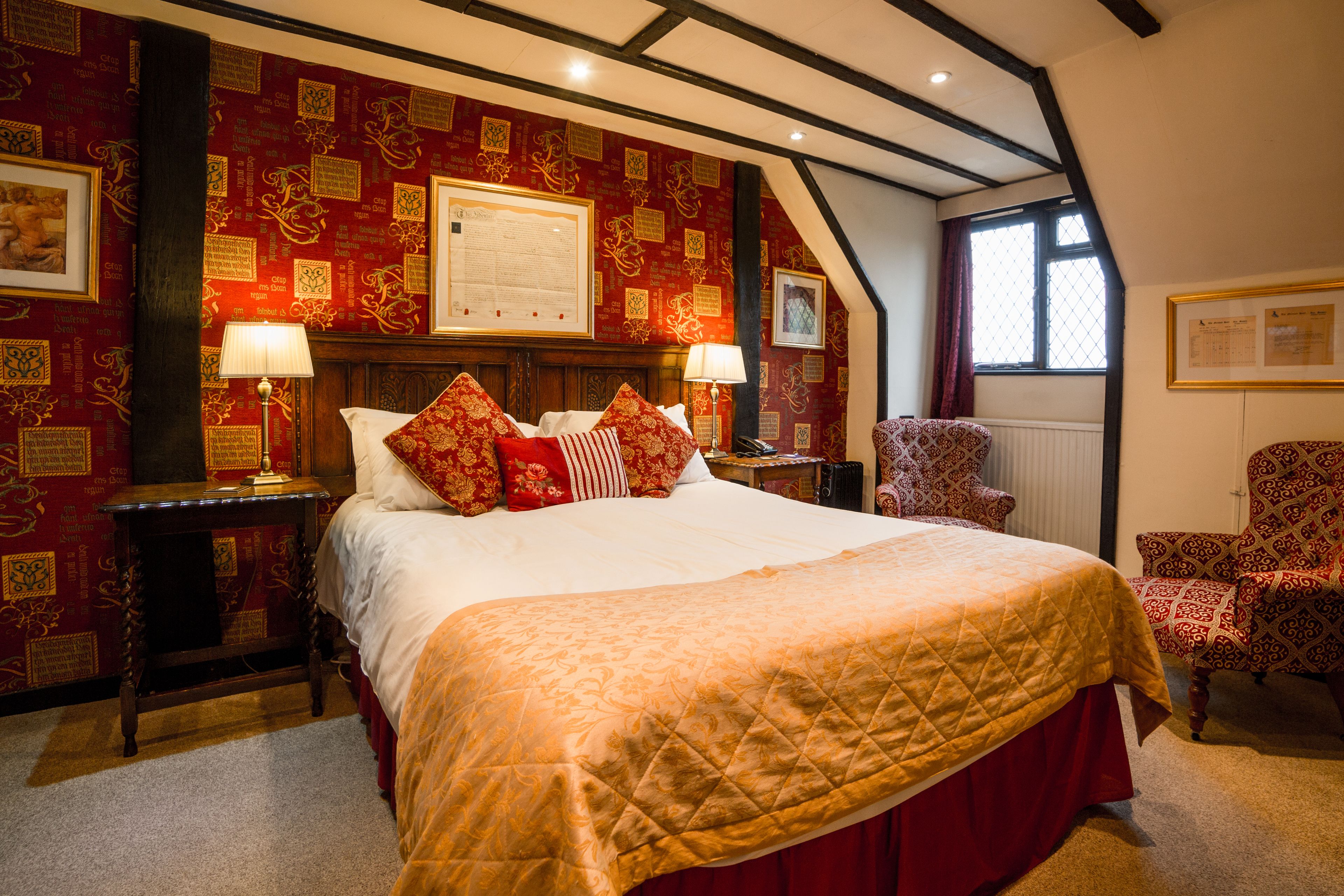 A traditional room with a large bed, two bedside tables, a chair, and a window with curtains.