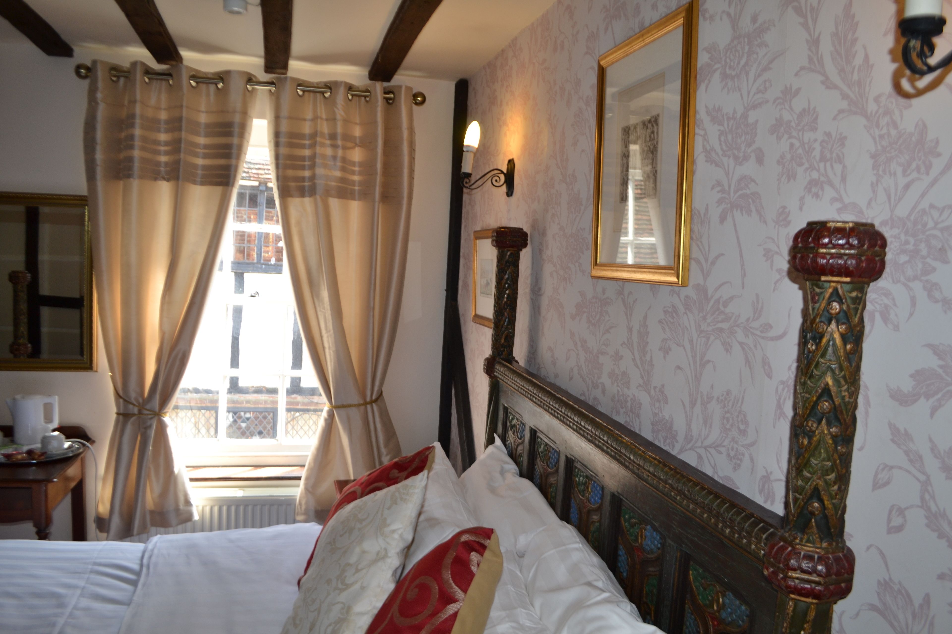 Un dormitorio con una cama grande, cabecera de madera, un espejo y una ventana con cortinas.