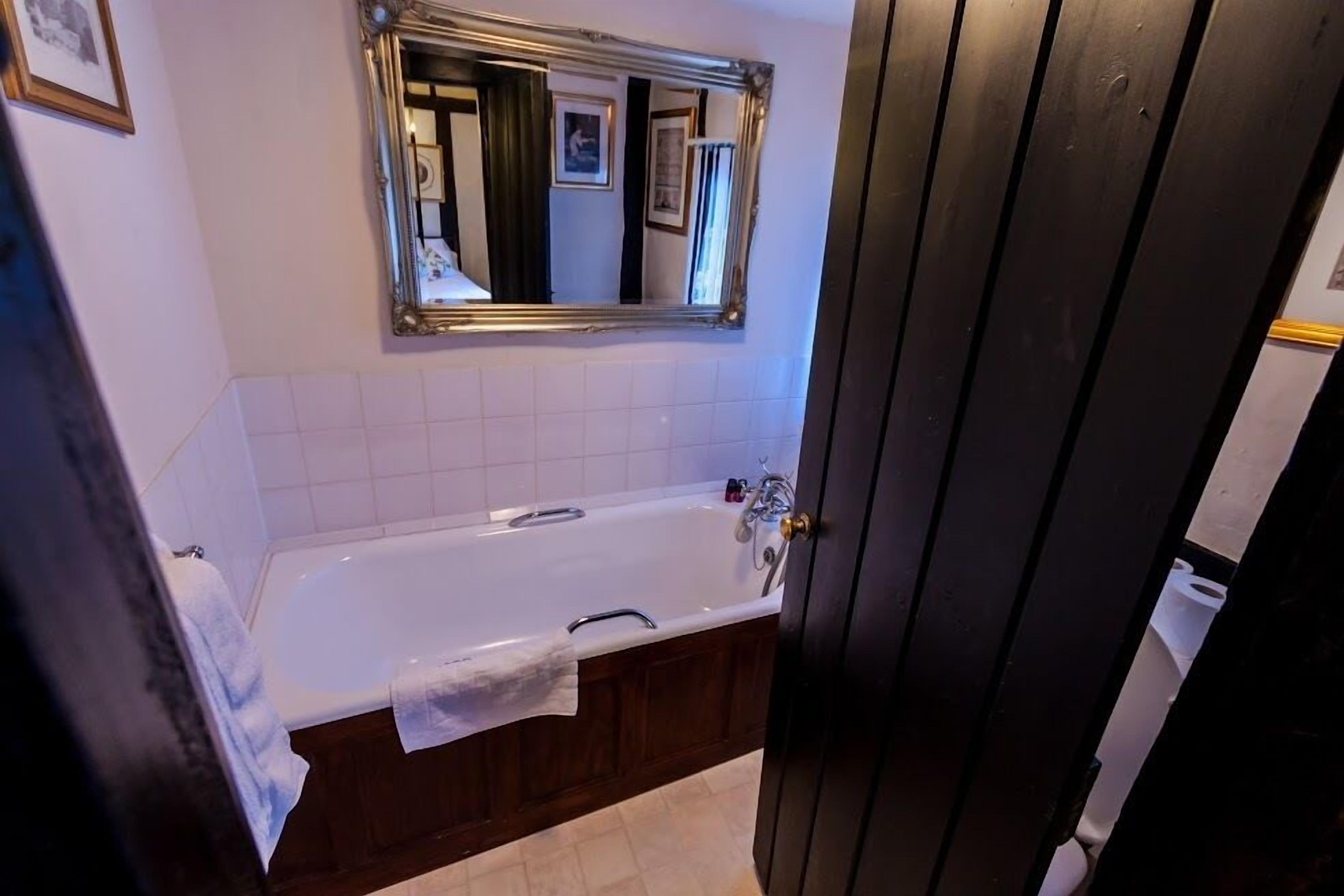 A bathroom with a white bathtub, a mirror above it, and a wooden door.