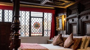 A traditional bedroom with a four-poster bed, a large window with a stained glass design, and ornate wooden furniture. - The Mermaid Inn (Rye)