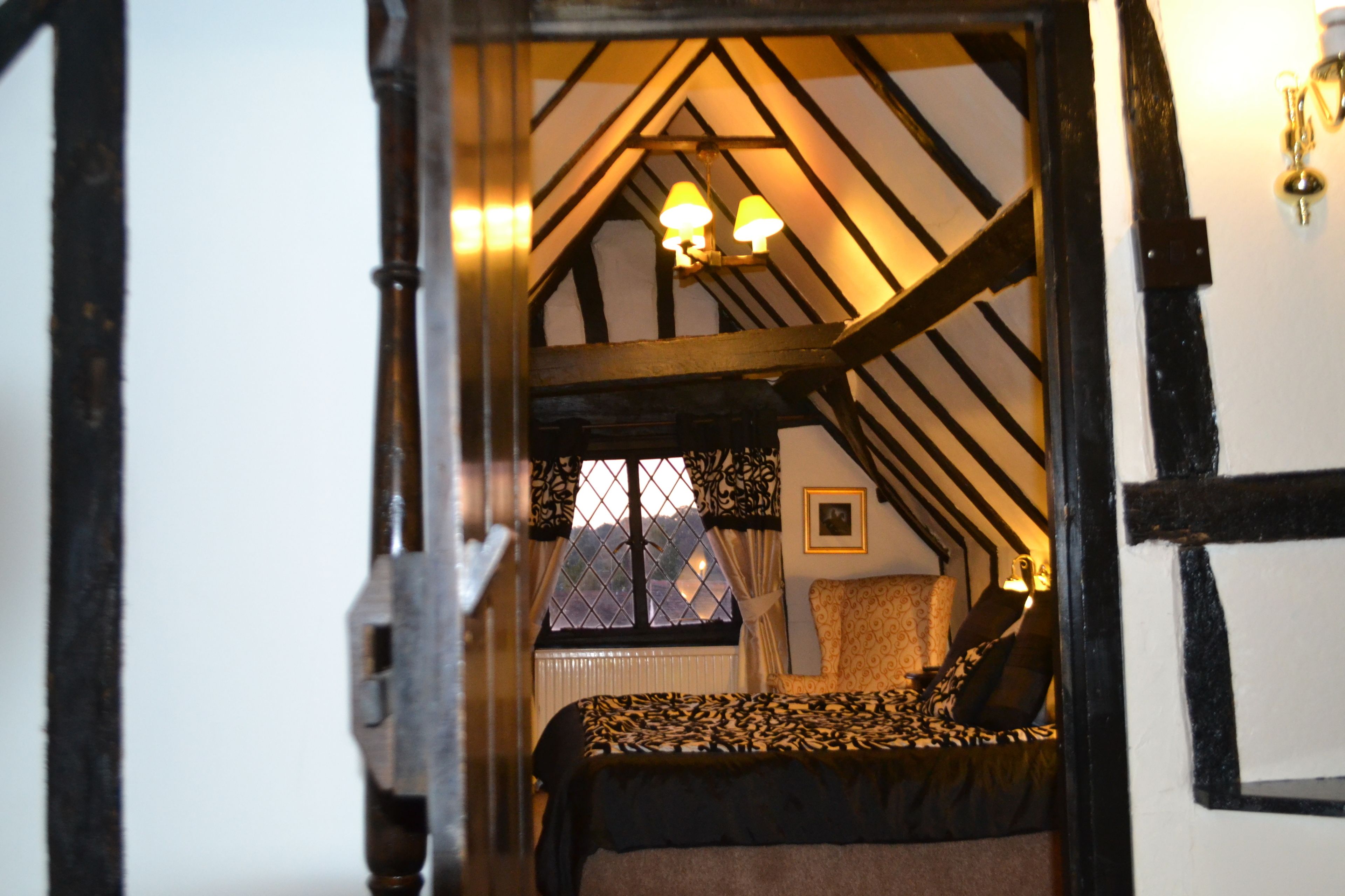 A bedroom with a bed, a window with curtains, a chandelier, and a view of the outside.