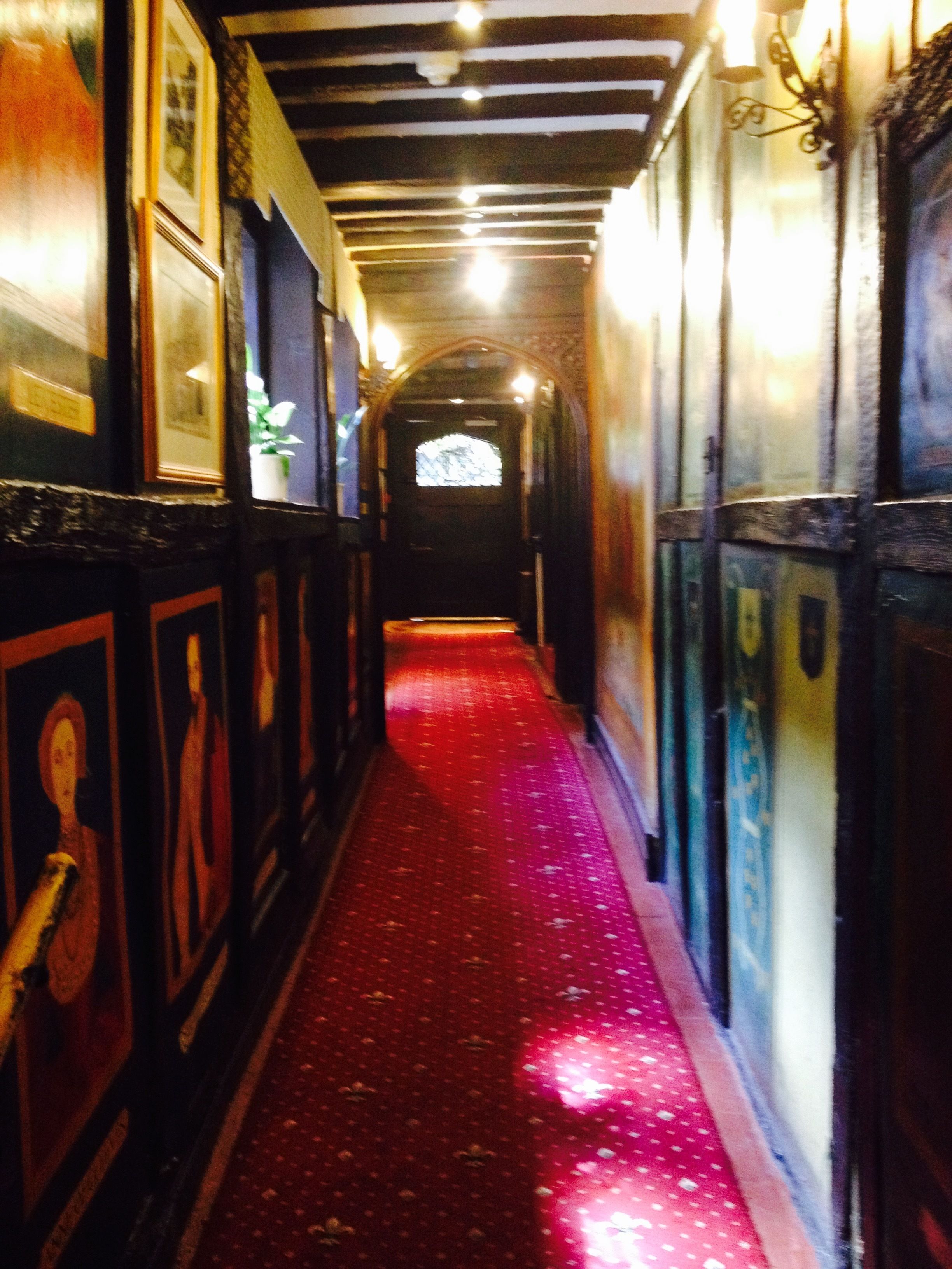 Un couloir étroit, doté d’une moquette rouge, de murs en bois et d’œuvres d’art encadrées.