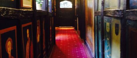 A narrow hallway with a red carpet, wooden walls, and framed artwork.