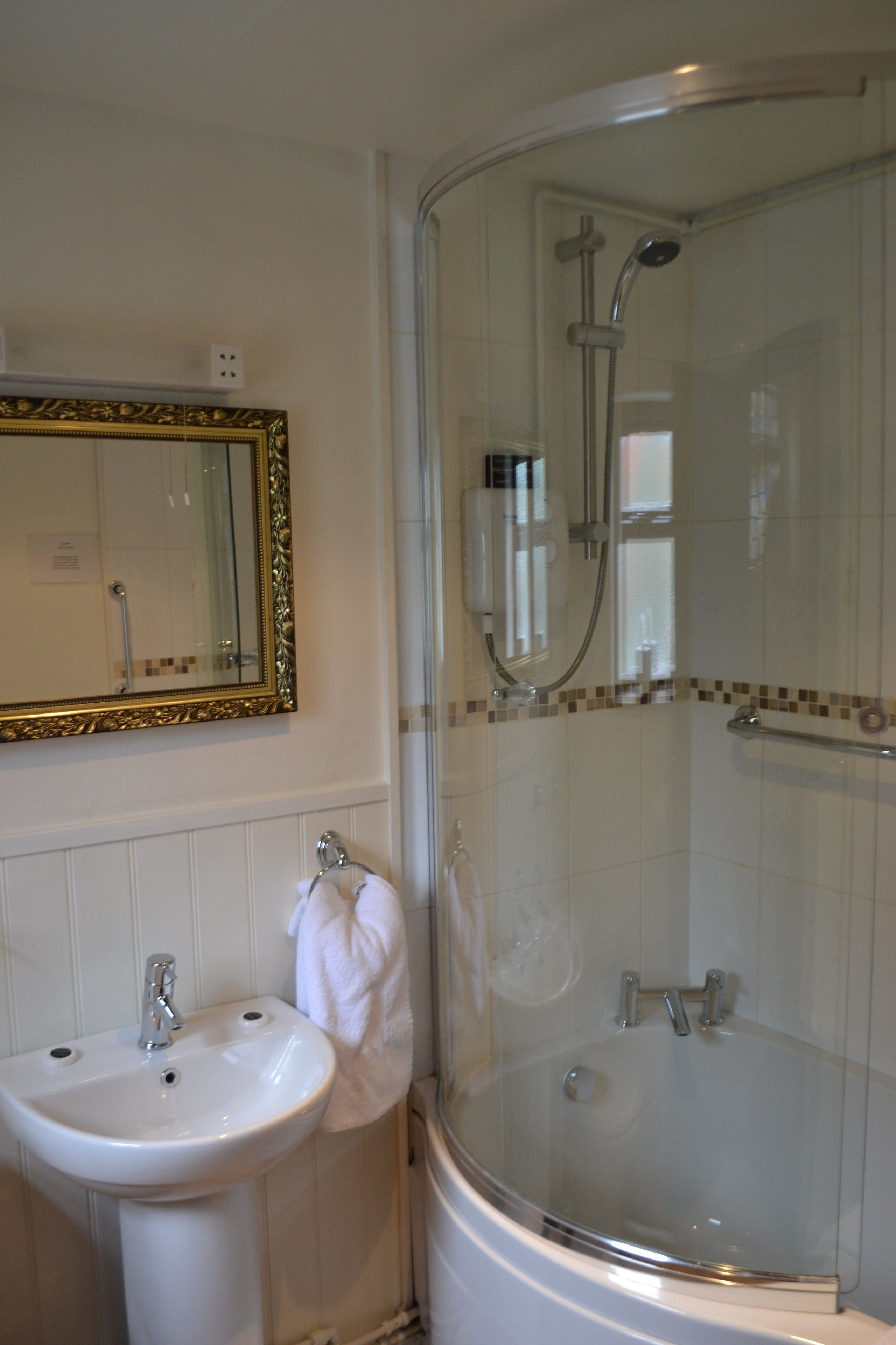 A bathroom with a white sink, a mirror with a gold frame, and a glass-enclosed shower area.