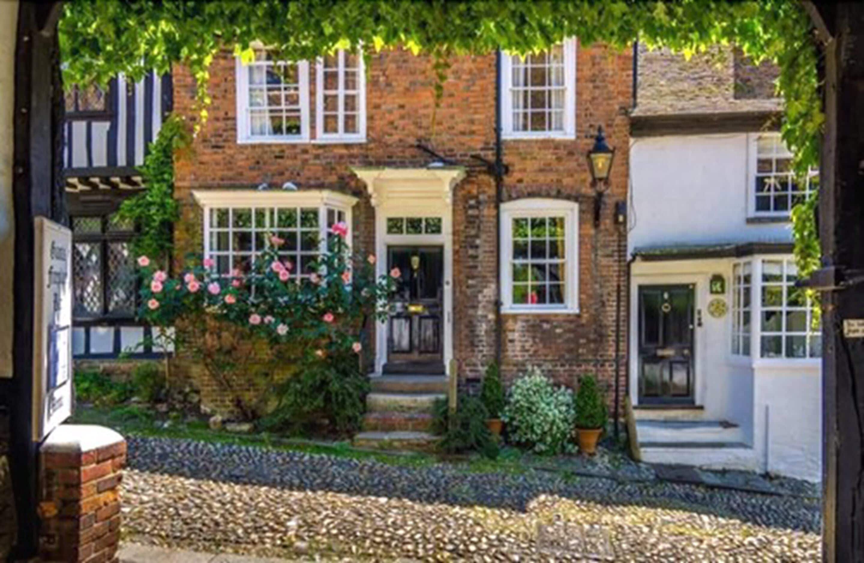 A traditional brick building with a garden entrance, white-framed windows, and a cobblestone pathway.