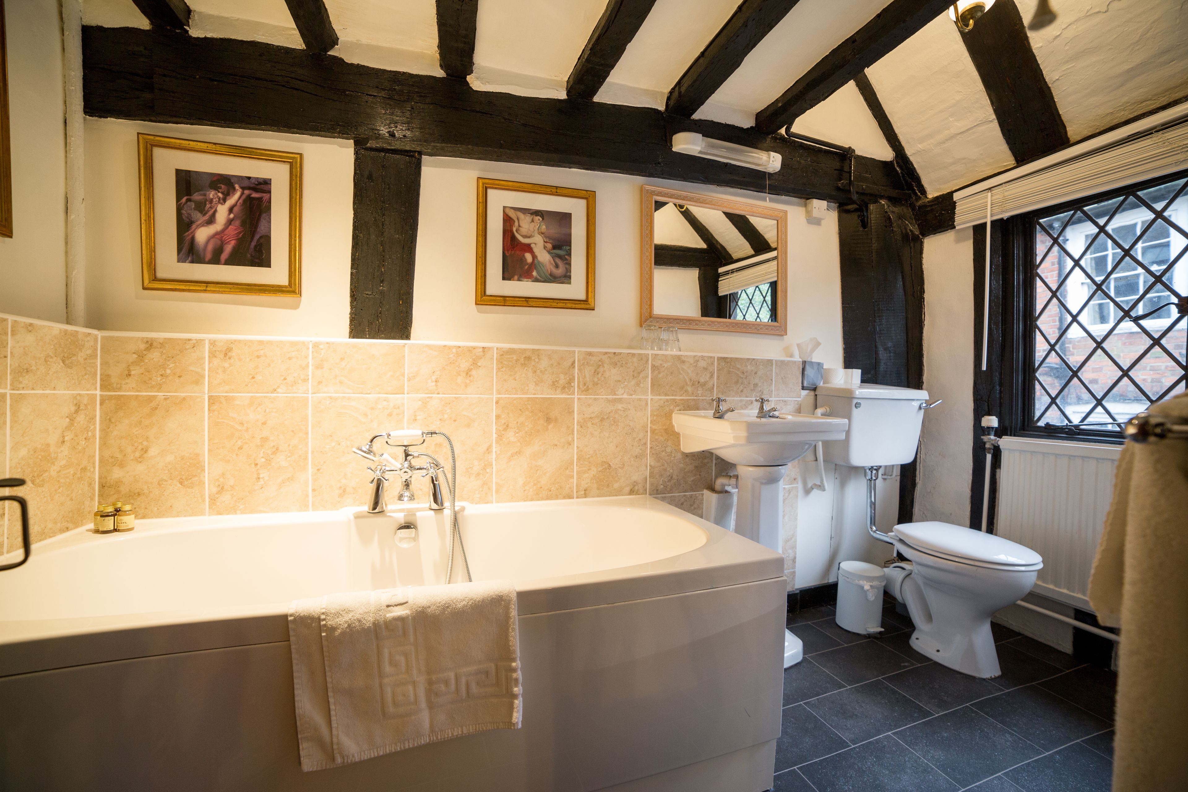 A bathroom with a freestanding bathtub, a sink, and a toilet. There are framed pictures on the wall above the bathtub.