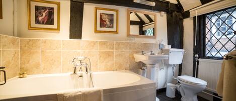 A bathroom with a freestanding bathtub, a sink, and a toilet. There are framed pictures on the wall above the bathtub.