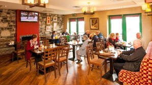A restaurant with wooden tables and chairs, stone walls, and framed pictures on the walls. - The Arches Hotel (Galway)