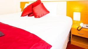 A hotel room with a bed, red pillows, a bedside table with a phone, and a wall-mounted light. - The Arches Hotel (Galway)
