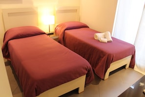 Dos camas individuales con ropa de cama roja, una lámpara de noche y una toalla sobre una cama.