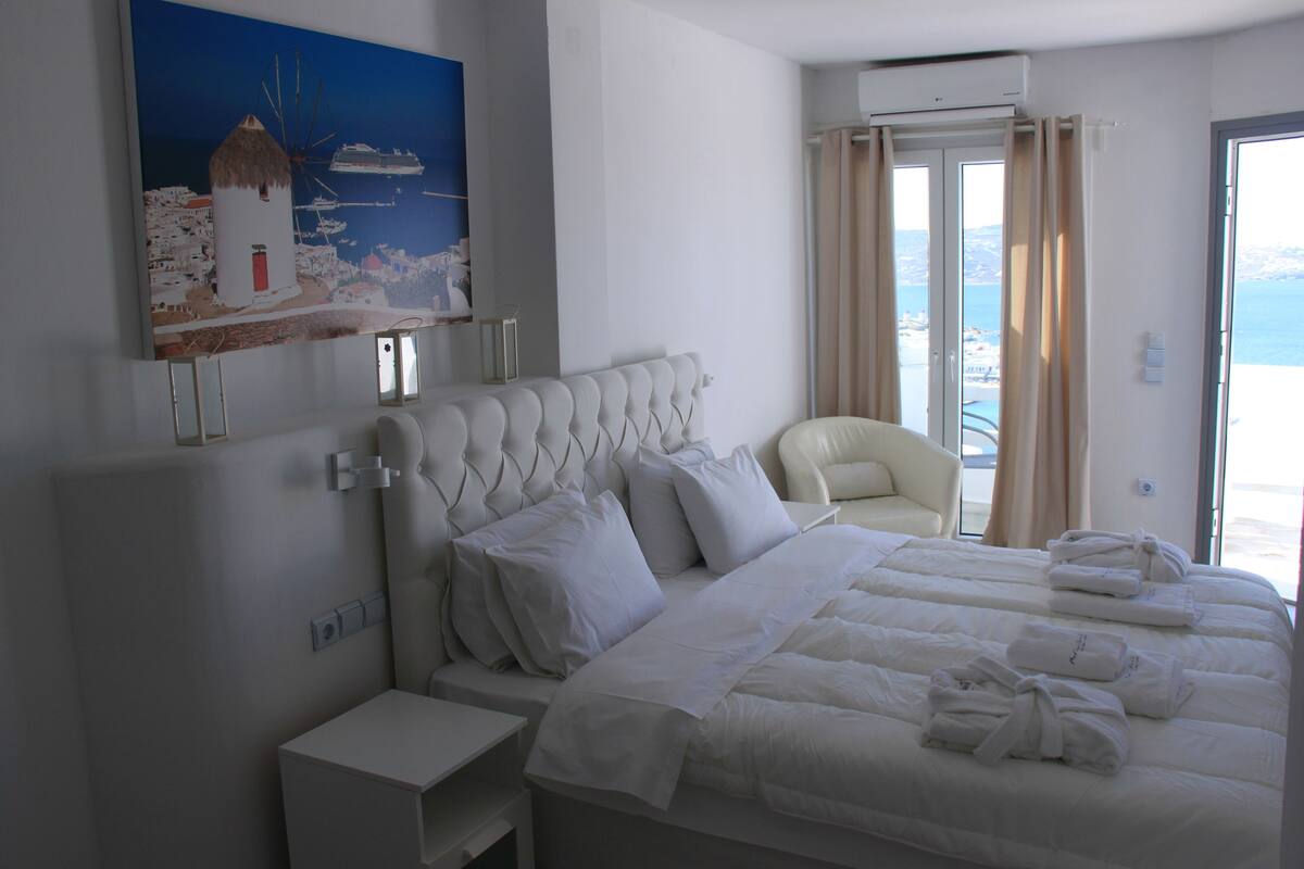 Ein Hotelzimmer mit einem großen Bett, einem Sessel, einem Gemälde und Blick aufs Meer.