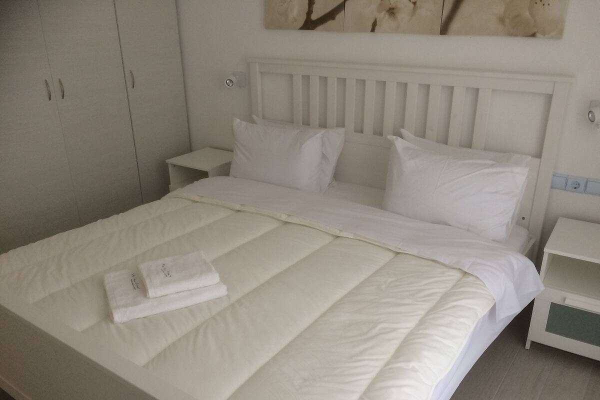 Ein ordentlich bezogenes Bett mit weißen Leinen, einem gefalteten Handtuch und einem weißen Kopfteil.