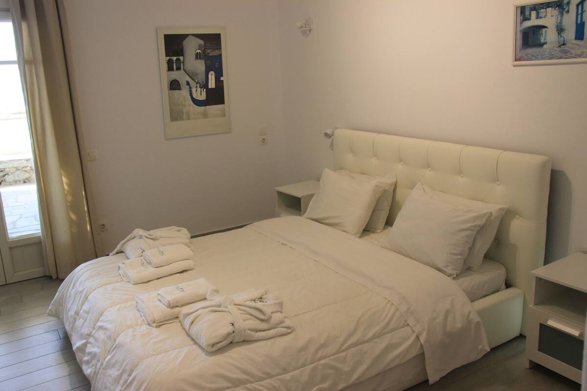 Ein großes Bett mit weißer Bettwäsche und Kissen, ein Nachttisch und ein gerahmtes Bild an der Wand.