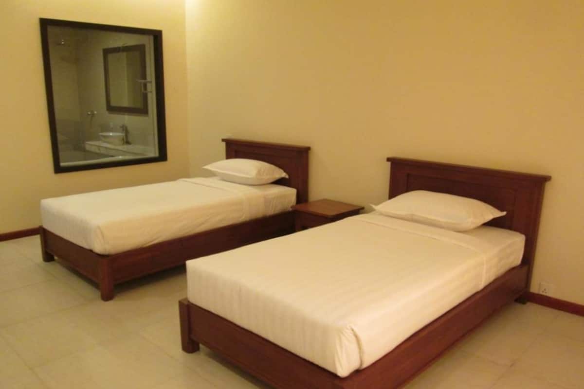 A hotel room with two single beds, a wooden headboard, a nightstand, and a mirror on the wall.