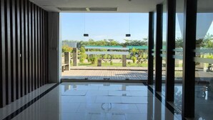 Un lobby moderno con piso reflectante, ventanas amplias y vistas a un área exterior con banco y follaje.