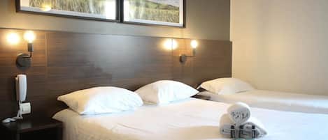 A hotel room with two beds, a wooden headboard, wall-mounted light fixtures, and framed pictures above the beds.