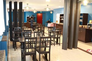 A restaurant with multiple tables and chairs, a red door, and a clock on the wall. - Hôtel Orly Superior (Athis-Mons)