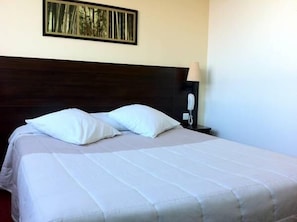 A neatly made bed with white bedding, a dark headboard, and a framed picture above it.