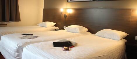 A hotel room with two beds, a nightstand, and a wall-mounted light fixture.