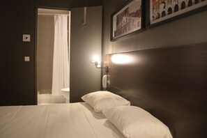 Una habitación de hotel con una cama, un teléfono en la mesita de noche y un cuadro en la pared.