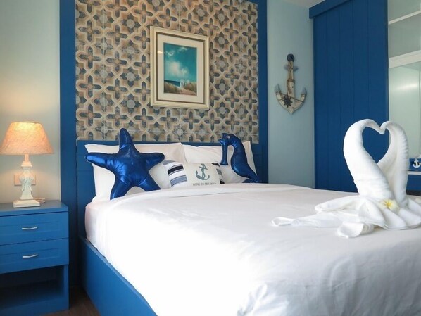 Una cama bien hecha con ropa de cama blanca y almohadas azules con forma de estrella, una pared con un diseño geométrico y una lámpara sobre una mesita de noche.
