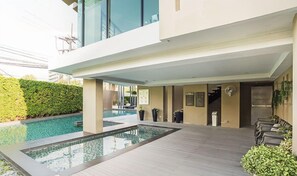 Un hotel moderno con zona de piscina, mobiliario exterior y un paseo cubierto.