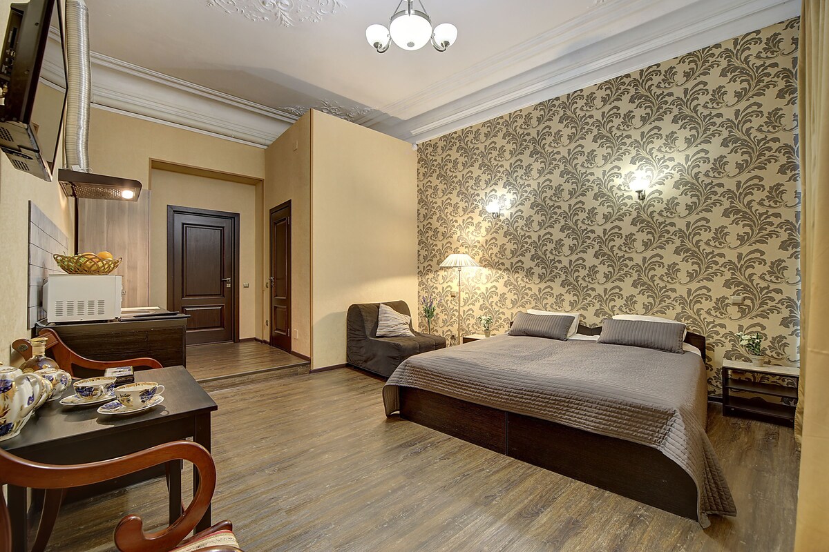 A hotel room with a bed, a desk with a lamp, a chair, and a dining table.