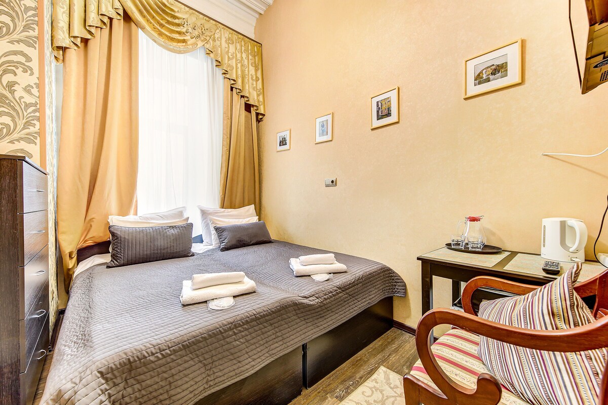 A hotel room with a bed, a desk, a chair, and a window with curtains.
