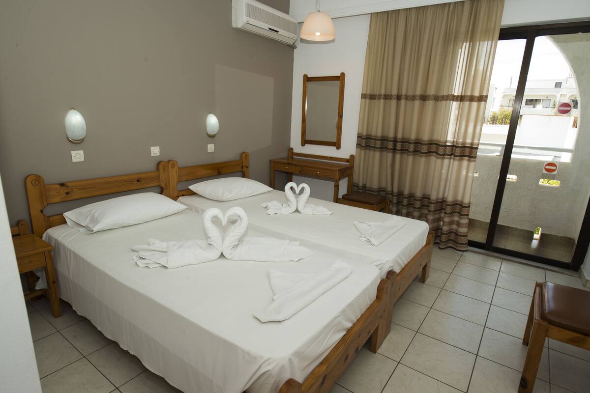 A hotel room with two wooden beds, white linens, a wooden nightstand, a mirror, and a view of the street through a glass door.