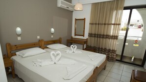 Habitación de hotel con dos camas de madera, sábanas blancas, una mesita de noche de madera, un espejo y vistas a la calle a través de un ventanal.