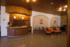 Un área de recepción con mostrador de madera, dos lámparas, un reloj y una zona de estar con sillones naranjas.