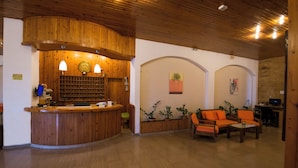 Un'area reception con un bancone in legno, due lampade, una sveglia e un angolo salotto con poltrone arancioni.